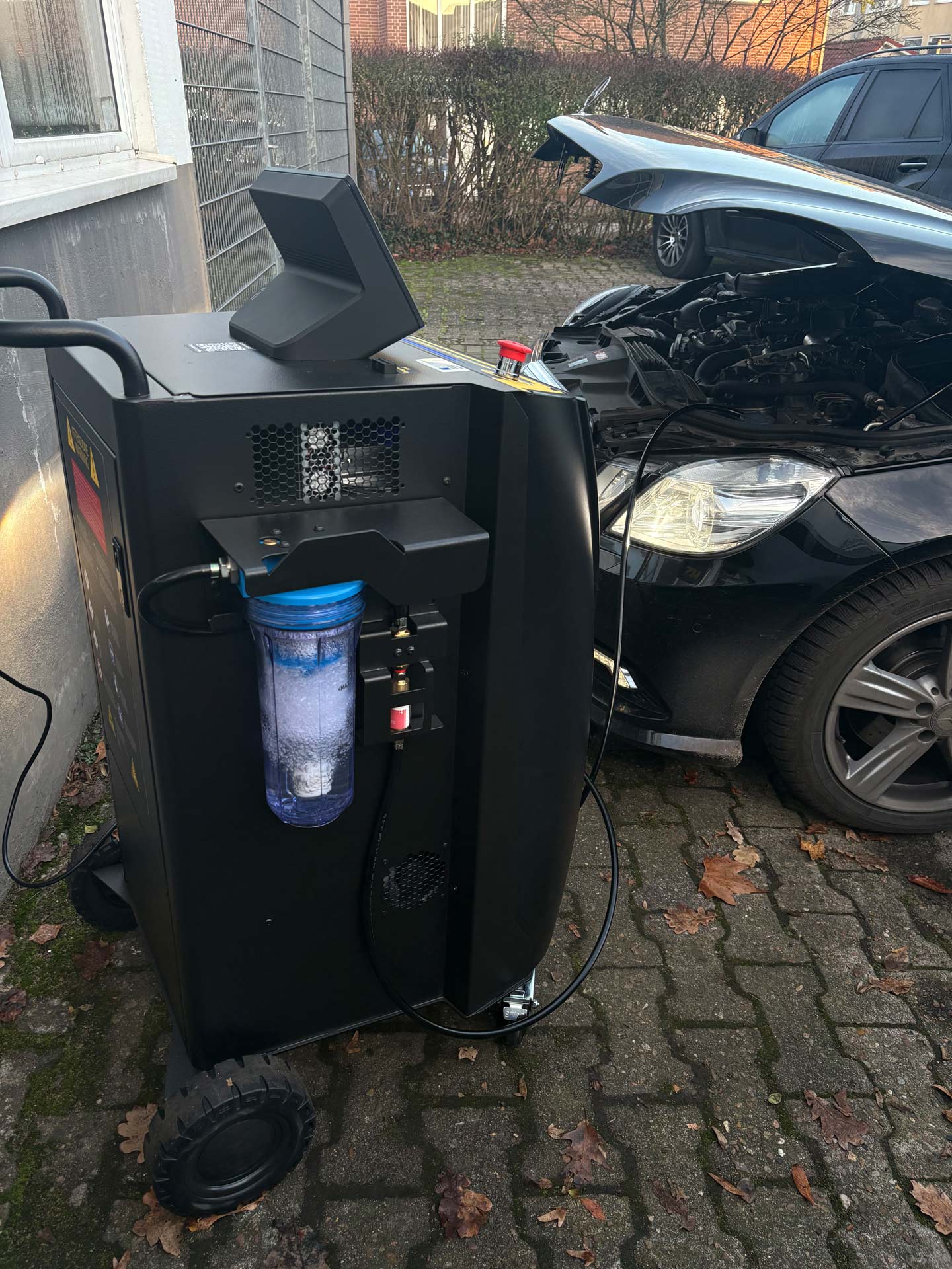 Ein schwarzes Gerät mit blauem Filter steht neben einem Auto mit offener Motorhaube