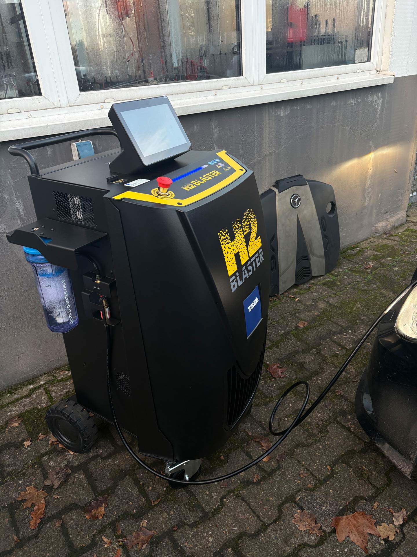 Ein schwarzer H2 Blaster mit blauem Wasserfilter und Touchscreen steht auf Pflastersteinen